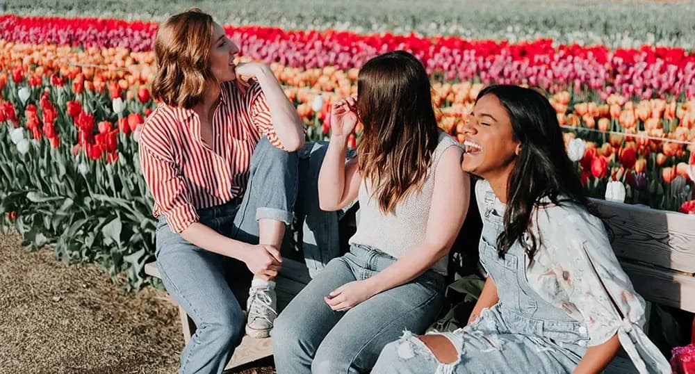 Three young women sit on a bench in tulip field