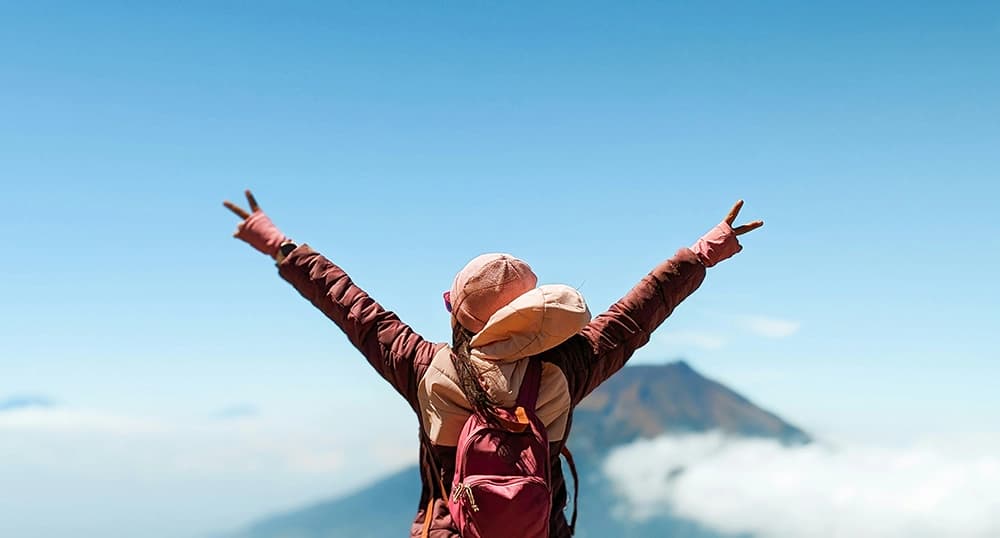 Budget traveler holding up peace signs on top of mountain.