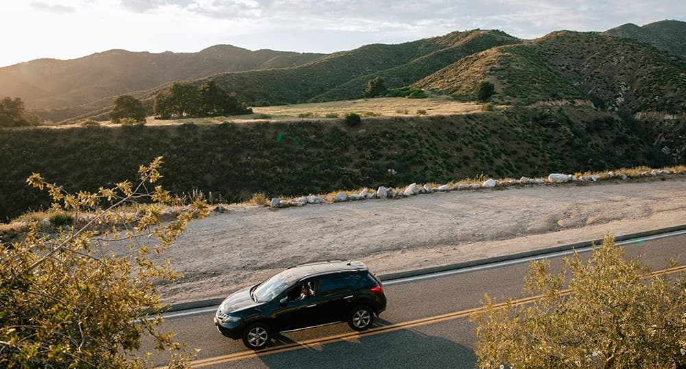 Car driving on a highway through rolling hills.