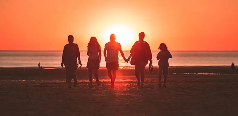 Family of 5 walking on a beach at sunset.
