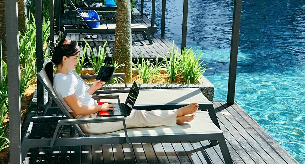 Female digital nomad working on a laptop next to a pool.