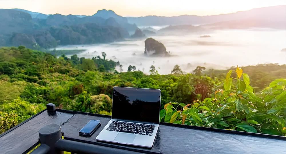Laptop sits on a counter overlooking tropical coastline