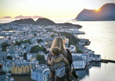 Woman with a baby in a backpack overlooks a scenic bay.