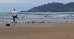 One-legged man with crutches stands on beach