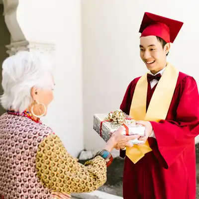Man in red graduation gown gives gift to grandmother