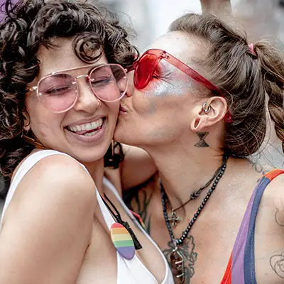 Lesbian couple celebrating PRIDE with a kiss at the parade downtown.