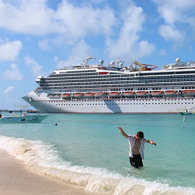 Person wading in ocean next to cruise ship.
