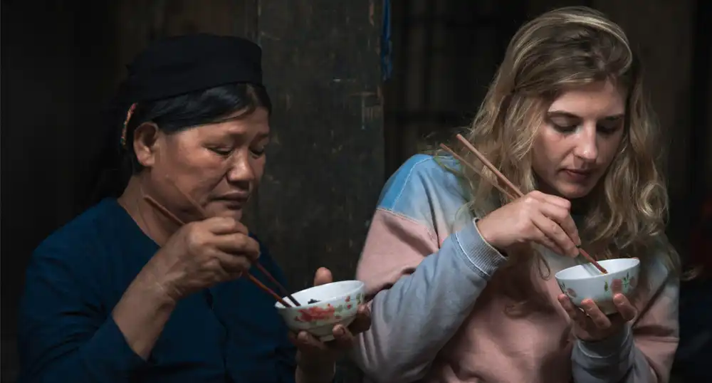 Tourist eats with chopsticks with local woman