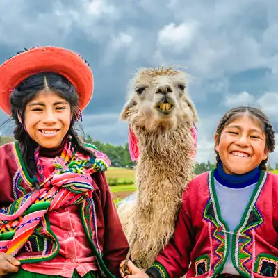 Two Peruvian girls stand smiling next to a llama