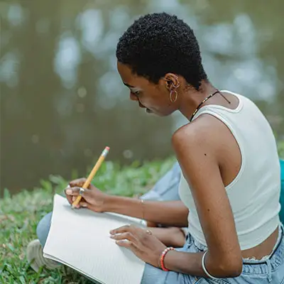 Millennial writing in her journal alongside a river.