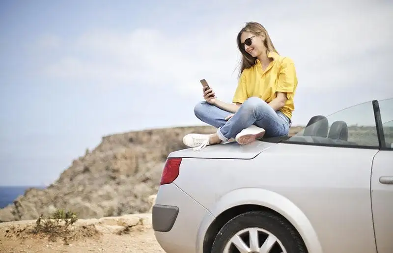 Student-sits-on-car-with-phone